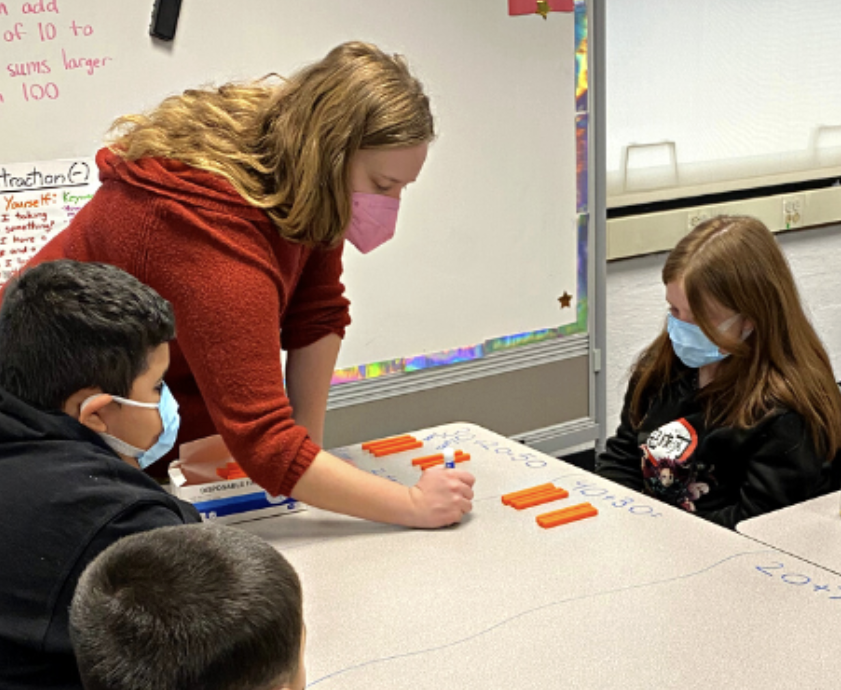 A math tutor works with a group of students on a whiteboard