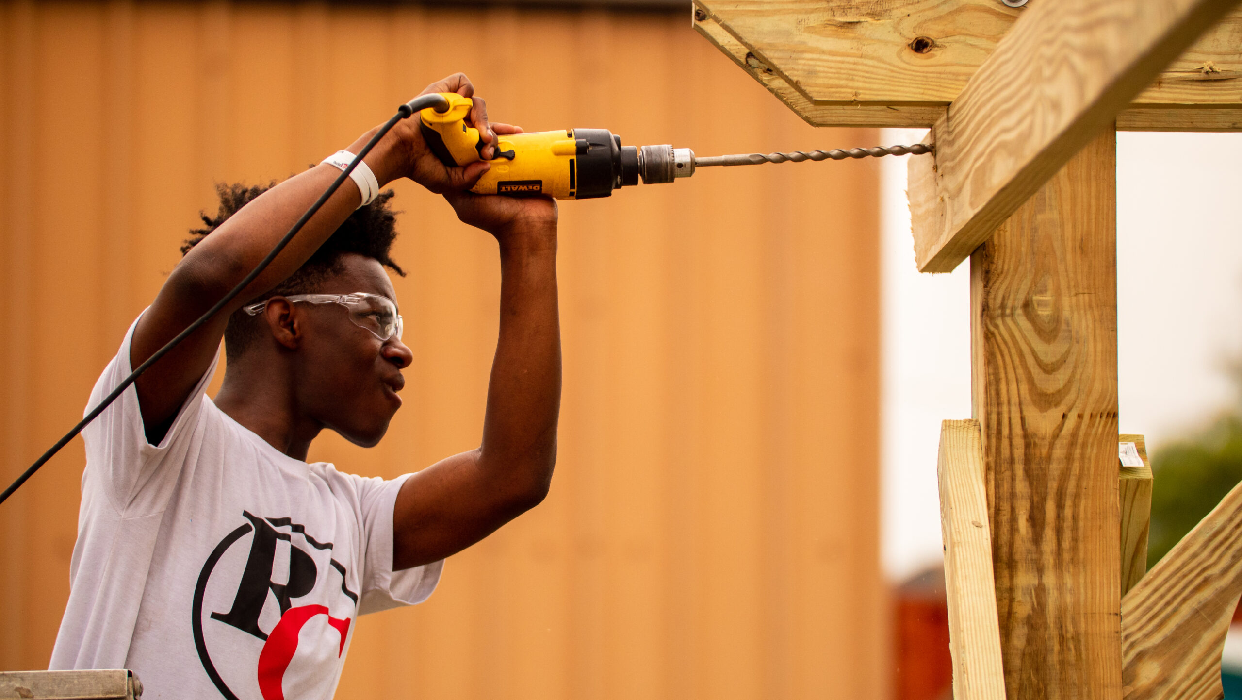 A young man uses a drill on the frame of a house