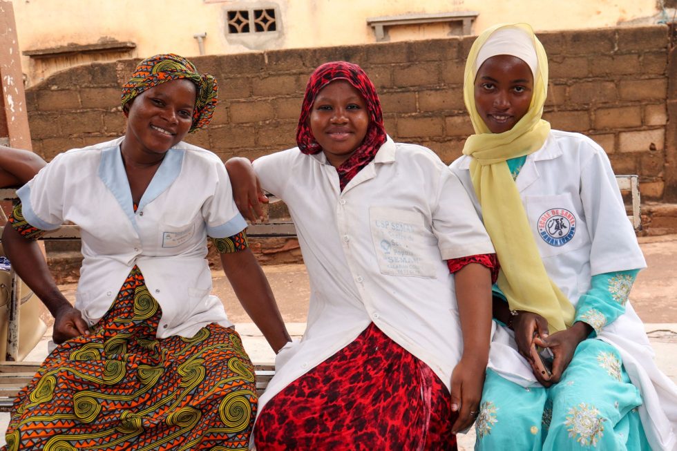 Three women wearing health worker uniforms smile